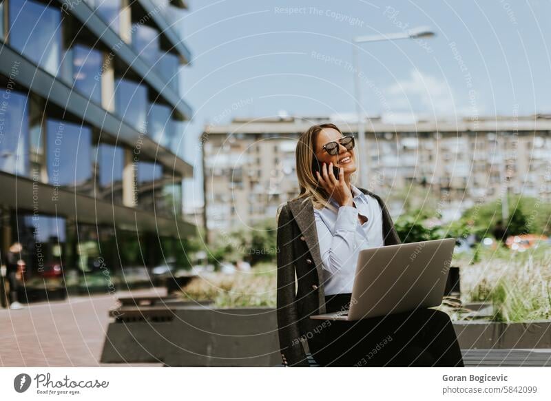Geschäftsfrau führt ein Gespräch vor einem modernen Bürogebäude, mittags Business professionell Arbeitsplatz Gebäude Laptop Smartphone außerhalb sonnig tagsüber