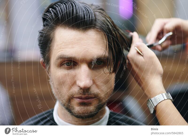 Serious man getting his wet hair cut in barbershop portrait serious bangs trim client comb sharp layer haircut section scissors rear back work hands brush