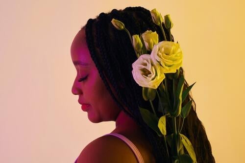 Calm Black woman with white roses in braided hair flower bloom romantic beauty blossom calm spring tender present birthday portrait face love hairstyle light