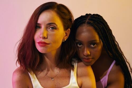 Portrait of beautiful Black and Caucasian women standing in neon light female beauty appearance best friend party woman confidence portrait diverse wellbeing