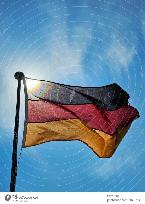 Die Flagge von Deutschland weht vor blauem Himmel mit leichten Wölkchen am Fahnenmast. Die Sonne scheint durch den Stoff. Deutschlandfahne Deutsche Flagge