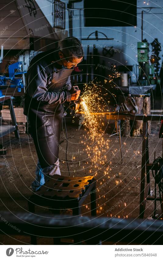 Handwerklicher Schmied bei der Arbeit mit Metall in einer Werkstatt Kunstgewerbler Hufschmied männlich Schleifen funkt Industrie manuell kompetent Wehen