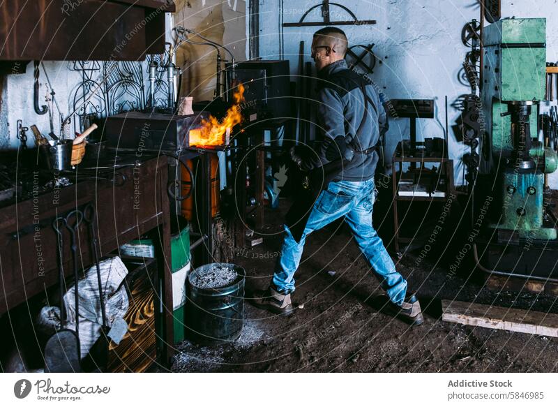 Anonymer Schmied bei der Arbeit mit heißem Metall in einer Schmiede Hufschmied schmieden Feuer Werkstatt traditionell Handwerk Werkzeuge industriell