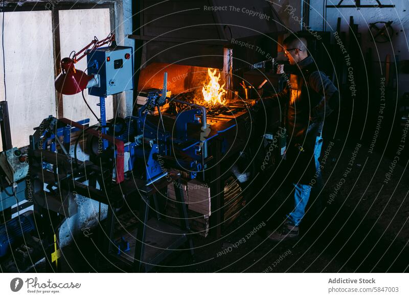 Männlicher Schmied bei der Arbeit an der Schmiede in einer dunklen Werkstatt Hufschmied männlich schmieden dunkel glühen heiß Metall Handwerk Handwerkskunst