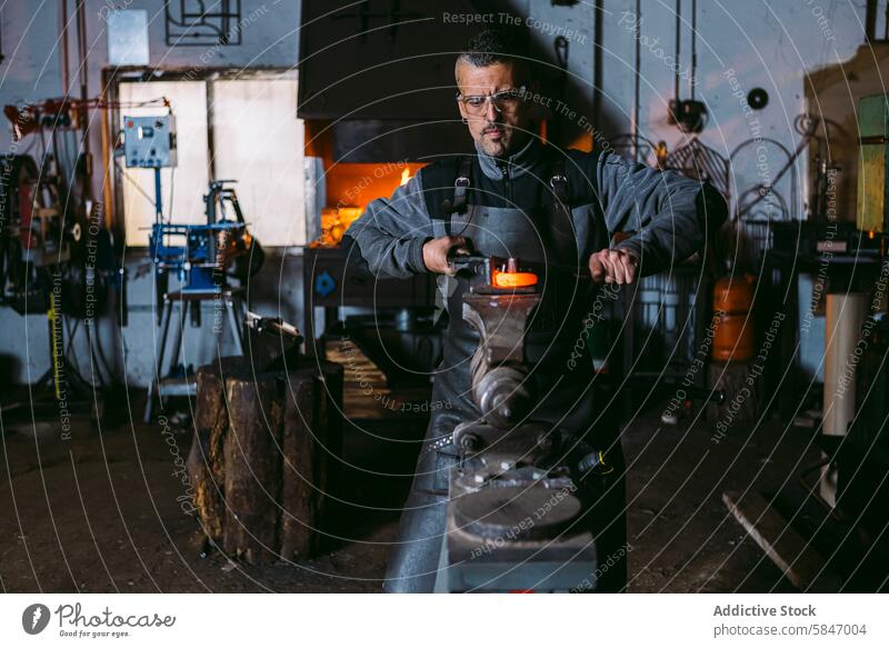 Schmied bearbeitet heißes Metall am Amboss in der Werkstatt Hufschmied männlich Hammer glühen Schmelzofen traditionell schmieden Formierung Arbeit Handwerk