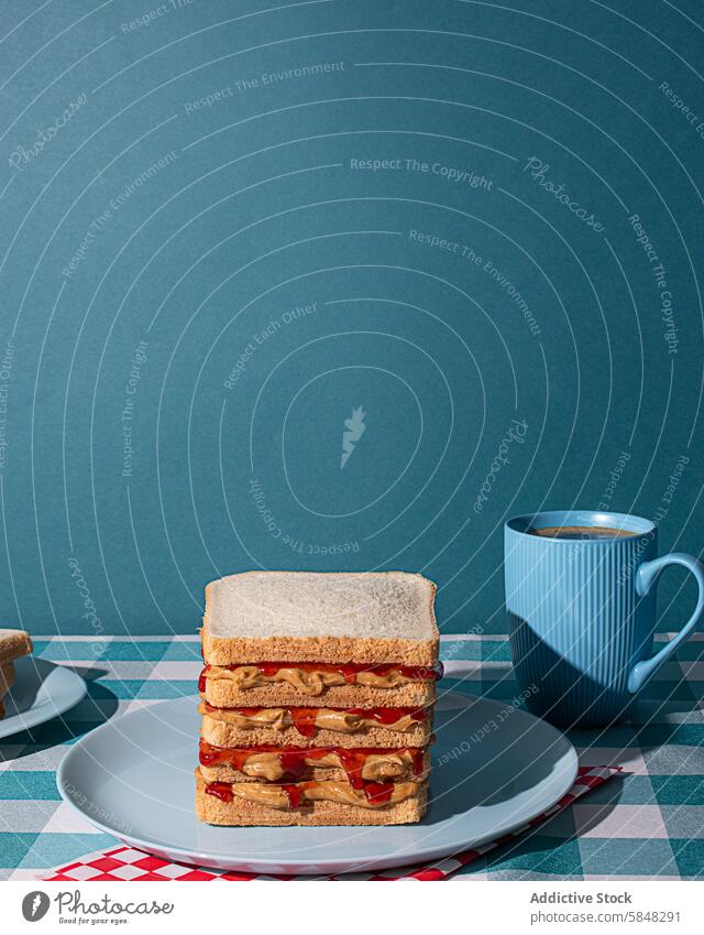 Leckere Erdnussbutter und Gelee-Sandwiches auf einem blauen Teller serviert, mit einer Tasse eines amerikanischen Kaffee und einige Brotscheiben in einem blauen Hintergrund