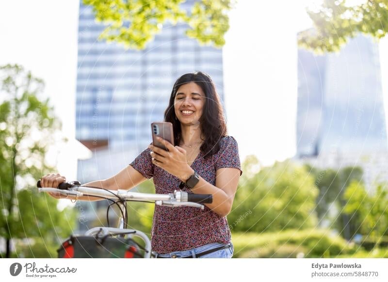 Junge Frau benutzt ihr Smartphone, während sie mit dem Fahrrad durch die Stadt fährt Inder echte Menschen Großstadt Spaß Sommer genießend Straße reisen