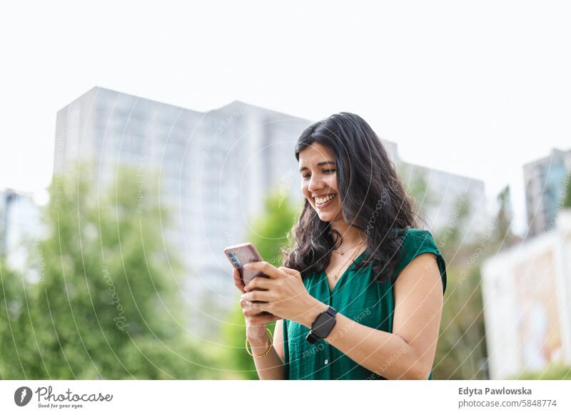 Lächelnde junge Frau benutzt ihr Smartphone in der Stadt Inder echte Menschen Großstadt Spaß Sommer genießend Straße reisen im Freien urban Erwachsener