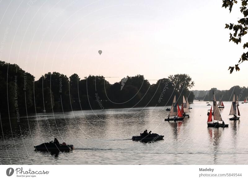 Bunte Segelboote und Jollen sowie ein Heißluftballon im Licht der Abendsonne auf dem Aasee in Münster in Westfalen im Münsterland Wochenende Abendstimmung