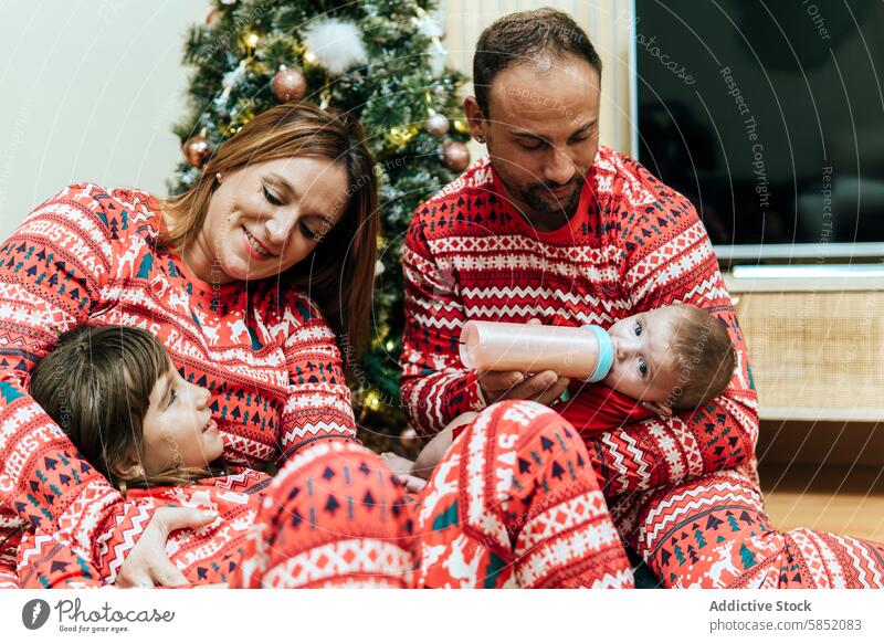 Gemütlicher Familienmoment während der Weihnachtsfeier Weihnachten Feier festlich Pyjama Vater Mutter Baby füttern Flasche Zuneigung Bonden Baum Feiertag