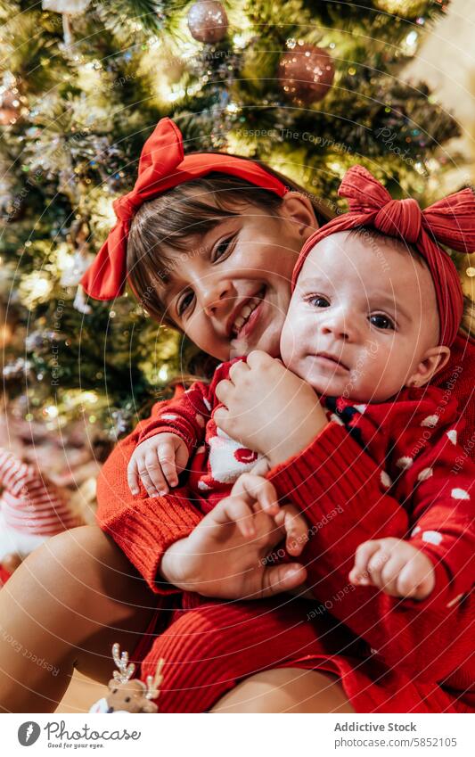 Geschwisterliebe während des Weihnachtsfestes Weihnachten festlich rot Baum dekoriert umarmend Freude Fotokamera Mädchen Baby Lächeln Schleife Outfit Stirnband