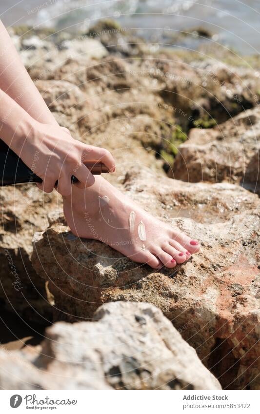 Person, die an einem felsigen Strand Sonnencreme auf die Füße aufträgt Sonnenschutz Haut Schutz Sonnenbad vereinzelt MEER Sommer Gesundheit Nahaufnahme