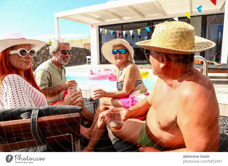 Fröhliche Senioren bei einer Zusammenkunft am Pool Schwimmbad Spaß Ruhestand Sonne Erholung Zuprosten Sammeln Freude lachen Sonnenbrille Hut Sommer Freizeit