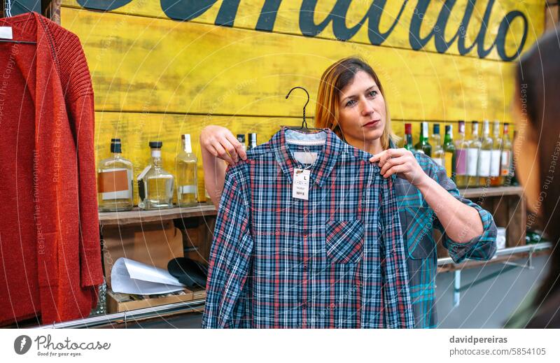 Freundliche Verkäuferin mit Sommersprossen zeigt einem Kunden im Laden ein kariertes Hemd. Werkstatt Assistent Frau zeigend Plaid Klient Verbraucher Blick