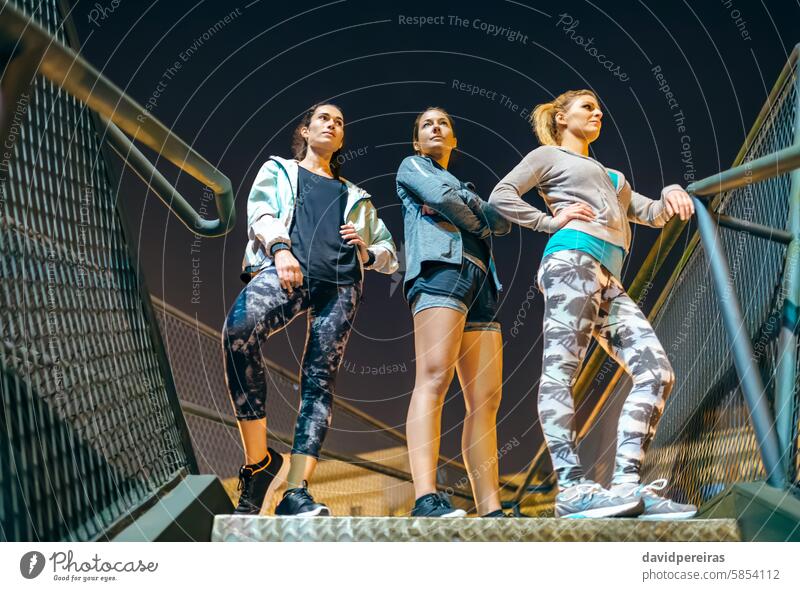 Drei Frauen stehen nachts auf einer städtischen Treppe, bereit für eine abendliche Trainingseinheit in der Stadt Athlet Läufer drei Stehen Treppenhaus Schritt