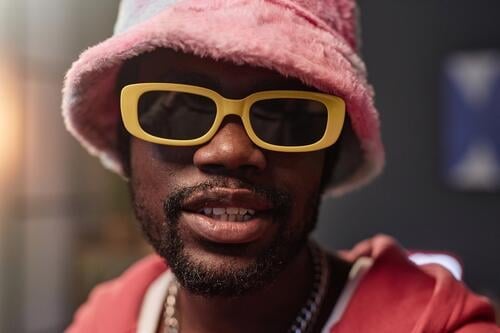 Schwarzer Mann mit Retro-Sonnenbrille und rosa Outfit Hiphop Rapper in die Kamera schauen Aufzeichnen Video Eimerhut Influencer Künstlerin soziale Netzwerke