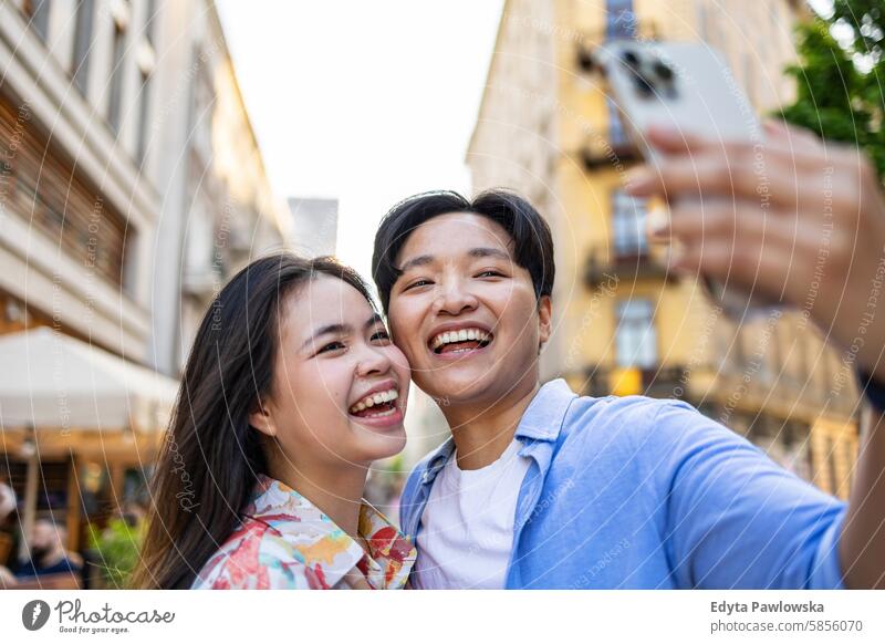 Lächelndes junges Paar beim Telefonieren in der Stadt asiatisch echte Menschen Spaß genießend junger Erwachsener authentisch heiter selbstbewußt Frau Glück