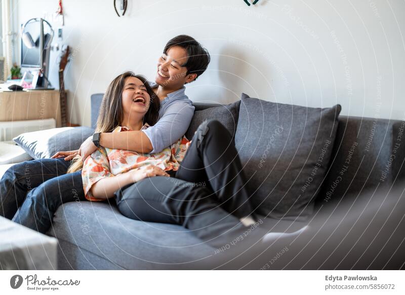 Lächelndes junges Paar entspannt sich auf dem Sofa asiatisch echte Menschen Spaß genießend junger Erwachsener authentisch heiter selbstbewusst Frau Glück Freude