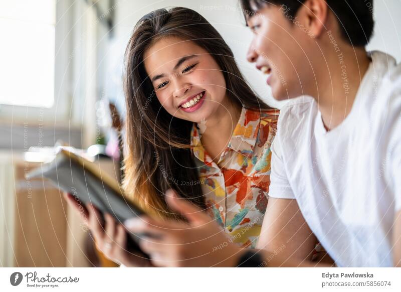Glückliches junges Paar, das gemeinsam auf dem Sofa zu Hause ein digitales Tablet benutzt asiatisch echte Menschen Spaß genießend junger Erwachsener authentisch