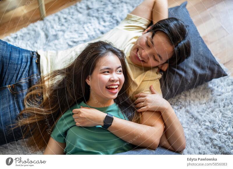 Glückliches junges Paar auf Teppich auf dem Boden liegend asiatisch echte Menschen Spaß genießend junger Erwachsener authentisch heiter selbstbewusst Frau