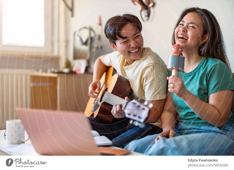 Glückliches junges Paar singt und spielt zu Hause auf der Gitarre asiatisch echte Menschen Spaß genießend junger Erwachsener authentisch heiter selbstbewusst