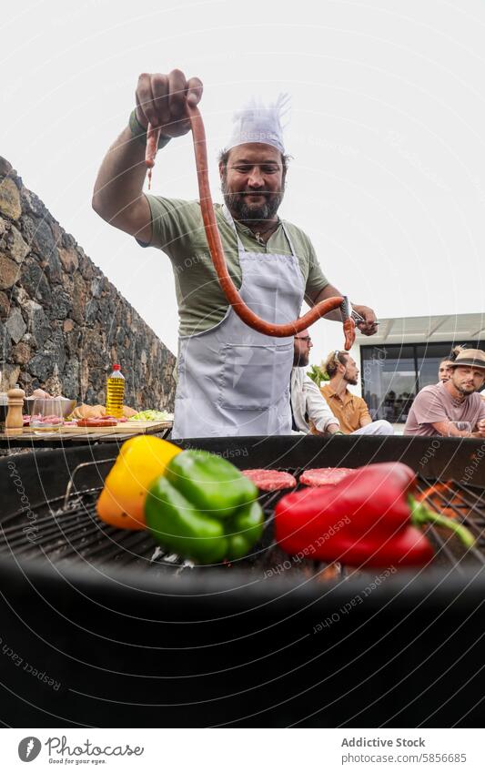 Chefkoch beim Grillen im Freien mit einer Gruppe von Freunden grillen Küchenchef Wurstwaren Fleisch multiethnisch Gespräch lässig freundlich Schürze Kochmütze