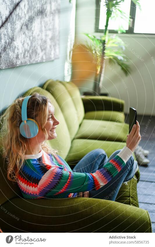 Junge Frau entspannt sich mit Kopfhörern und Smartphone entspannend Sofa grün heiter Musik Technik & Technologie jung Pause Raum lichtdurchflutet