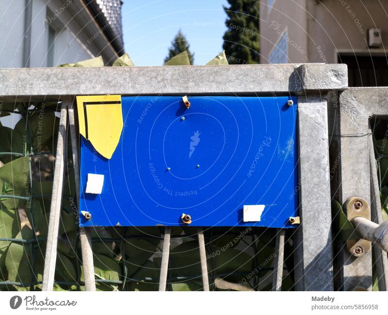 Blaue Tafel aus Kunststoff mit Resten eines gelben Hinweisschild am Hoftor eines Eigenheim bei Sonnenschein in Oerlinghausen bei Bielefeld am Hermannsweg ihn Teutoburger Wald