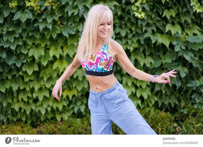 Frau, die sich durch Tanz neben einem städtischen Garten ausdrückt blond niedlich jung Ausdruck Glück Tanzen urban freudig energetisch Bewegung Lächeln