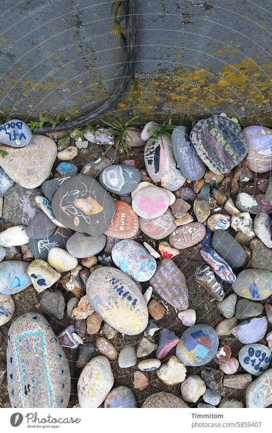 Steine, Grüße, Gedanken… Kieselsteine bemalt beschriftet verziert bunt Erinnerungen Außenaufnahme Wand Kabel Moos Menschenleer Dänemark Farbfoto