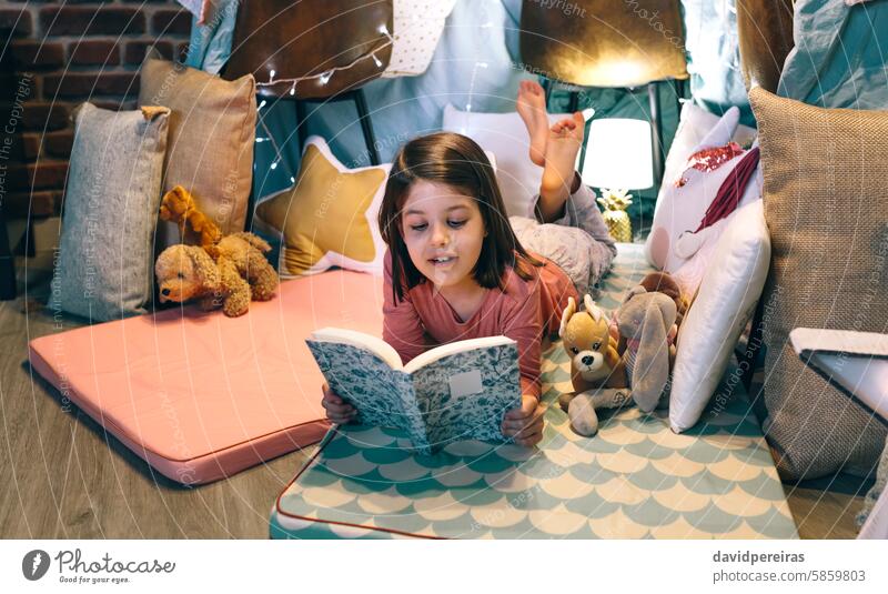 Glückliches kleines Mädchen beim Lesen und Entspannen auf der Schlafmatte in einem gemütlichen Zelt zu Hause lesen Buch Lügen Unterlage Schlafmatratze