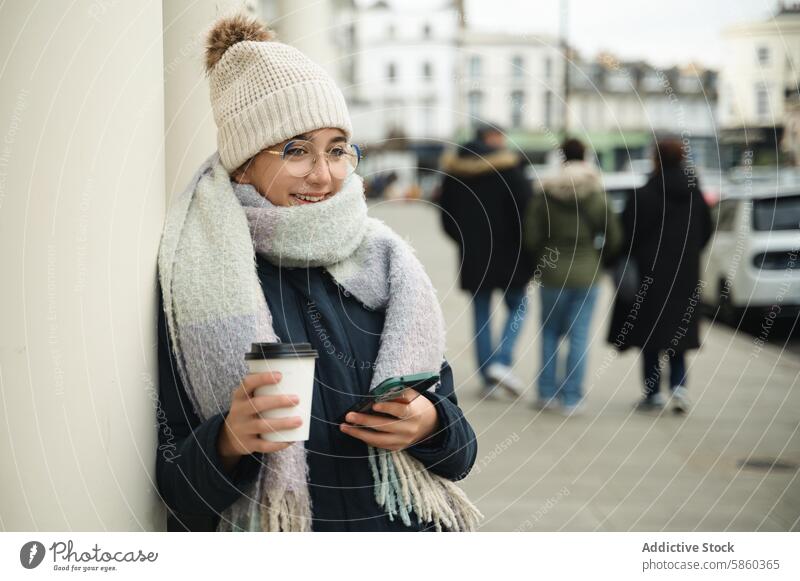 Lächelnde Frau mit Kaffee und Smartphone auf einer Londoner Straße Mode Accessoire Winter Technik & Technologie Stadtleben urban Brille Schal Hut trinken