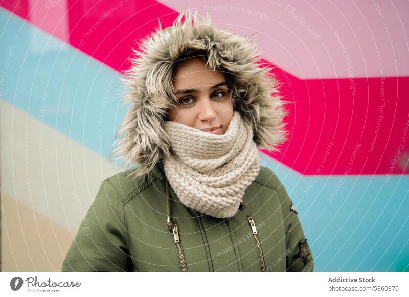 Junge Frau in gemütlicher Winterkleidung mit buntem Hintergrund Bekleidung Fell entgittern Kapuze Schal stricken Lächeln farbenfroh geometrisch warm Mode Stil