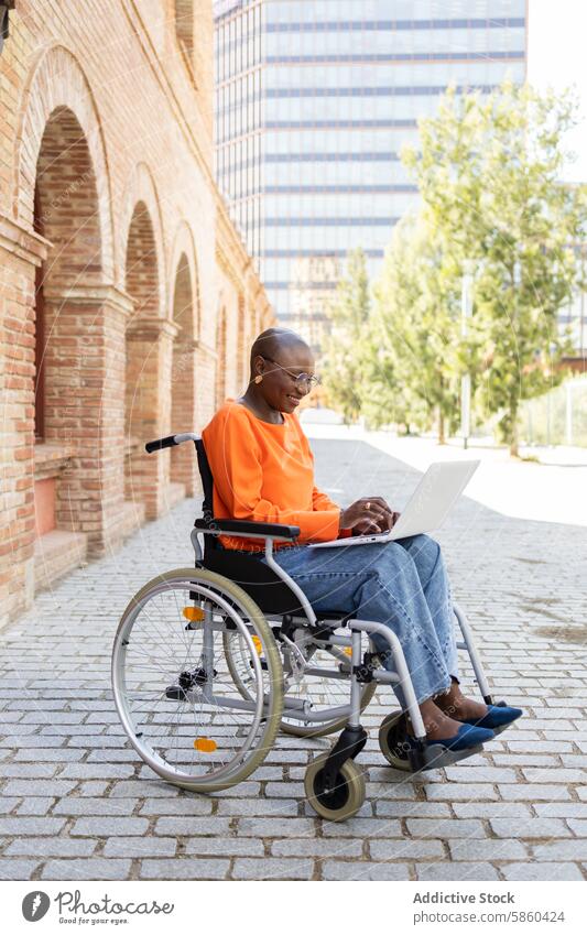 Afroamerikanische Frau arbeitet vom Rollstuhl aus in einer städtischen Umgebung Geschäftsfrau Laptop im Freien Zugänglichkeit Inklusivität modern Architektur