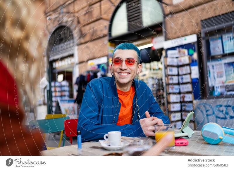 Junger Mann genießt einen Kaffee in einem Straßencafé in der Stadt jung im Freien Café Großstadt Lächeln digitales Gerät Buch urban Tisch blaue Haare