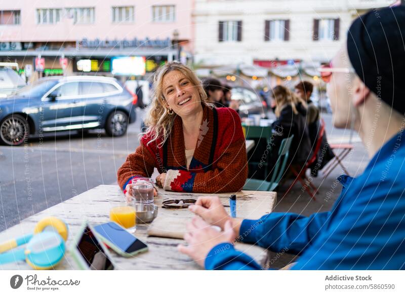 Ein Paar genießt ein fröhliches Gespräch in einem Café im Freien Frau Mann Lächeln urban Straße Tisch Diner PKW Pullover farbenfroh trinken Saft Wasser Sitzen