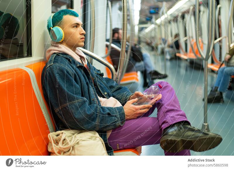 Junger Mann mit blauen Haaren genießt Musik in der U-Bahn jung blaue Haare Kopfhörer Smartphone heiter Jeansstoff Jacke purpur Hose öffentlicher Verkehr