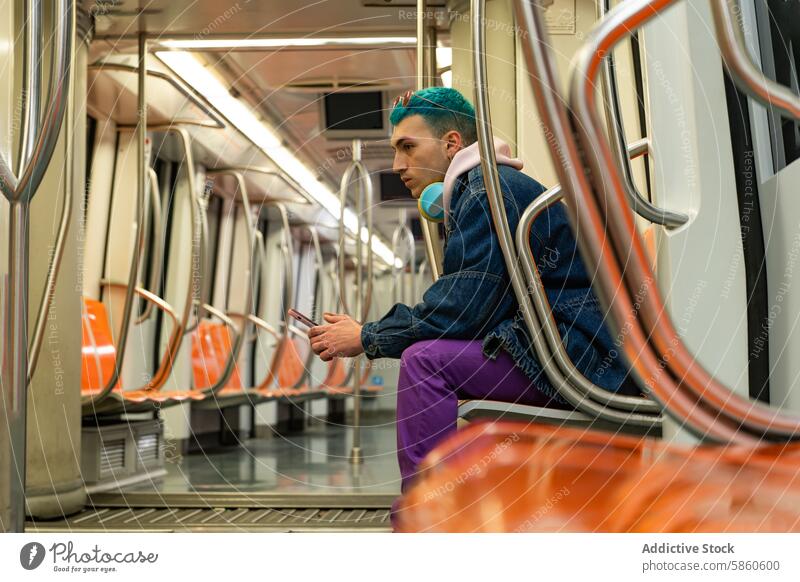 Junger Mann mit blauen Haaren genießt Musik in der U-Bahn jung blaue Haare Kopfhörer Smartphone heiter Jeansstoff Jacke purpur Hose öffentlicher Verkehr