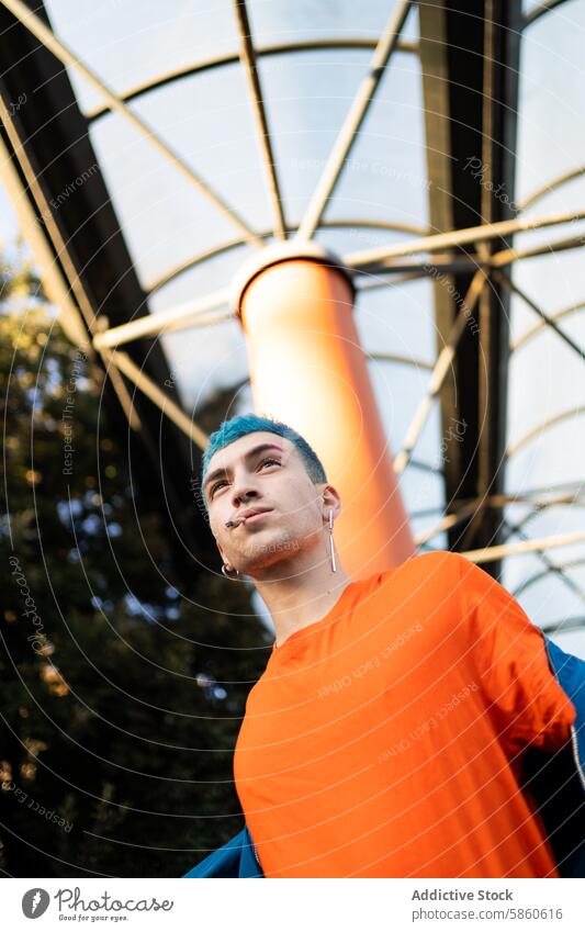 Junger Mann mit blauen Haaren in einem leuchtend orangefarbenen Hemd im Freien jung blaue Haare orangefarbenes Hemd modern stylisch geometrisch Architektur