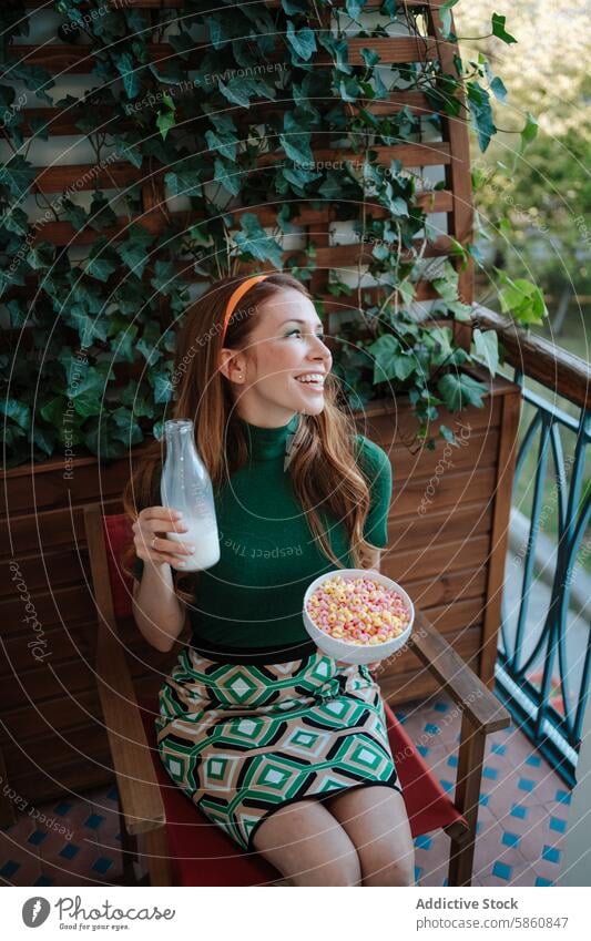 Retro inspirierte Frau genießt Müsli und Milch auf dem Balkon retro 1950s melken Mode Efeu grünes Kleid Sitzen Wegsehen Lächeln farbenfroh Frühstück