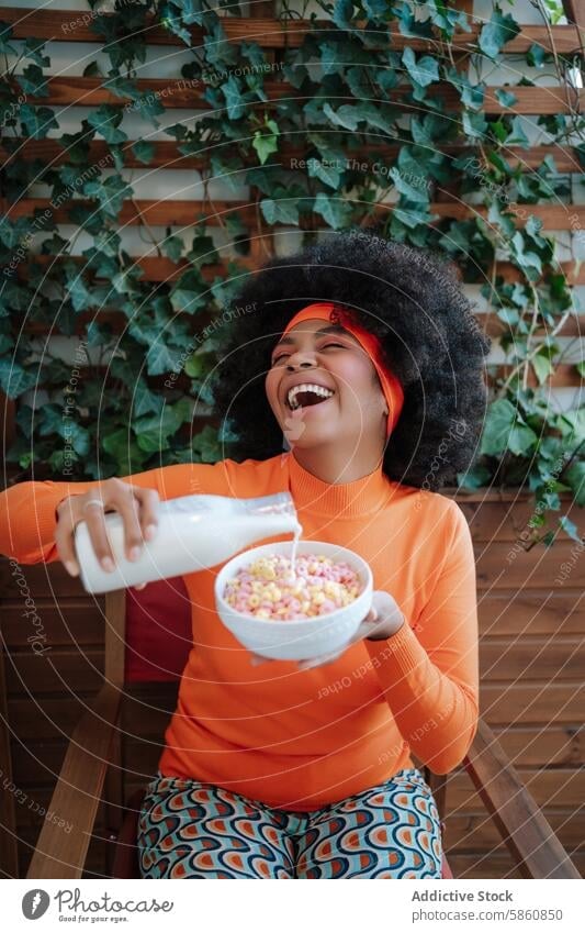 Lachende Frau im Retro-Outfit gießt Milch in eine Müslischale schwarz Afroamerikaner retro melken Schalen & Schüsseln Gießen Augen geschlossen Afrohaar