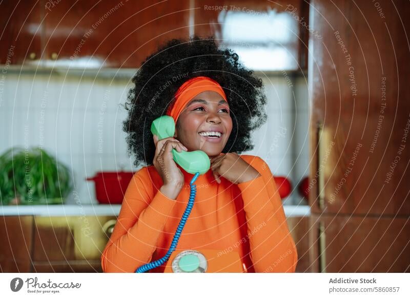 Fröhliche Hausfrau im Stil der 1950er Jahre plaudert am alten Telefon altehrwürdig 1950s freudig Küche orange schwarz Afroamerikaner Wegsehen Mode Nostalgie