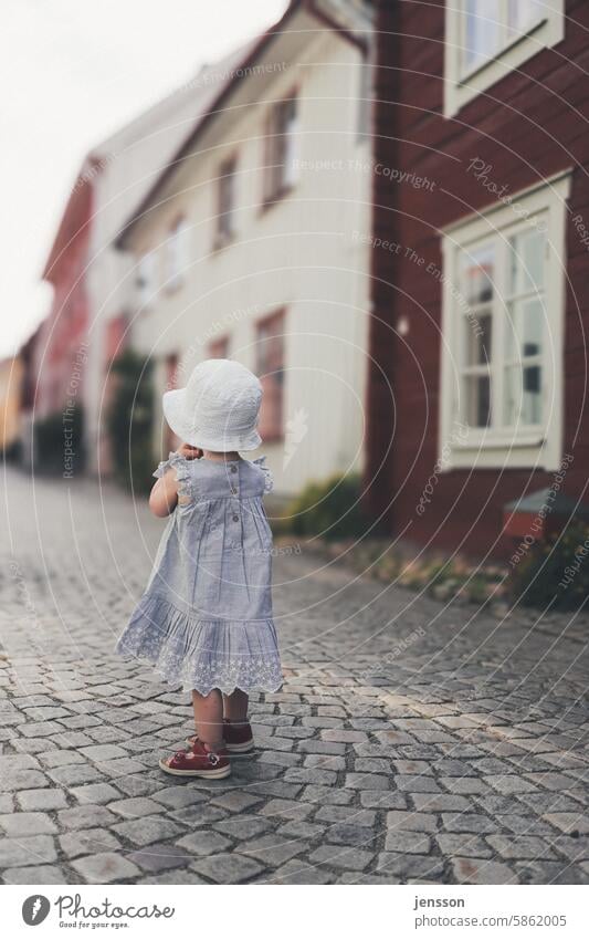 Ein kleines Mädchens steht auf einer Kopfsteinpflasterstraße und schaut in die Ferne Kind Kindheit Außenaufnahme Kleid junges Mädchen Kleinkind sommerlich