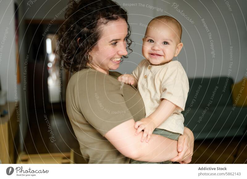 Glückliche Mutter hält ihr lächelndes Kleinkind zu Hause im Arm Lächeln Lachen heimwärts Familie Eltern Kind im Innenbereich Wohnzimmer Beteiligung Freude