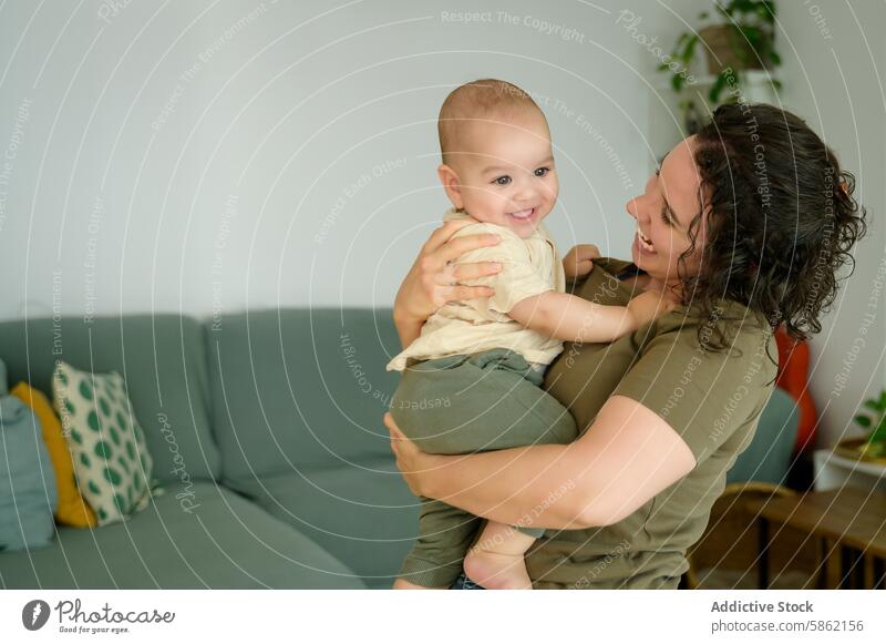 Mutter mit lockigem Haar hält ihr Baby im Wohnzimmer krause Haare Lächeln freudig Beteiligung Familie heimwärts im Innenbereich Fröhlichkeit Kind Frau Eltern