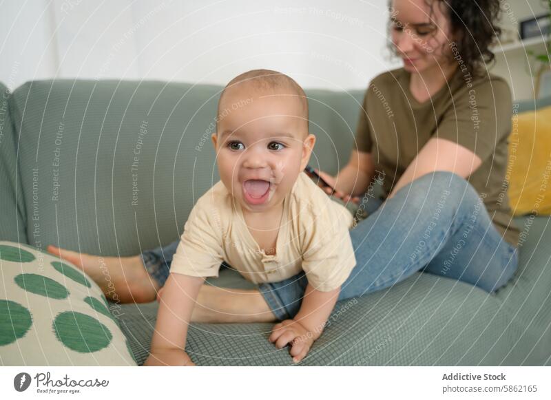 Mutter und Baby genießen die spielerische Zeit auf der Couch rassenübergreifend vielfältig Familie Sofa Handy Lächeln Wegsehen Kaukasier im Innenbereich