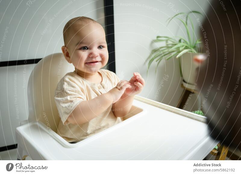 Baby im Hochstuhl lächelt den Vater aus dem Bild heraus an Lächeln verbindlich Erwachsener spielerisch Mann warm im Innenbereich Zimmerpflanze jauchzen