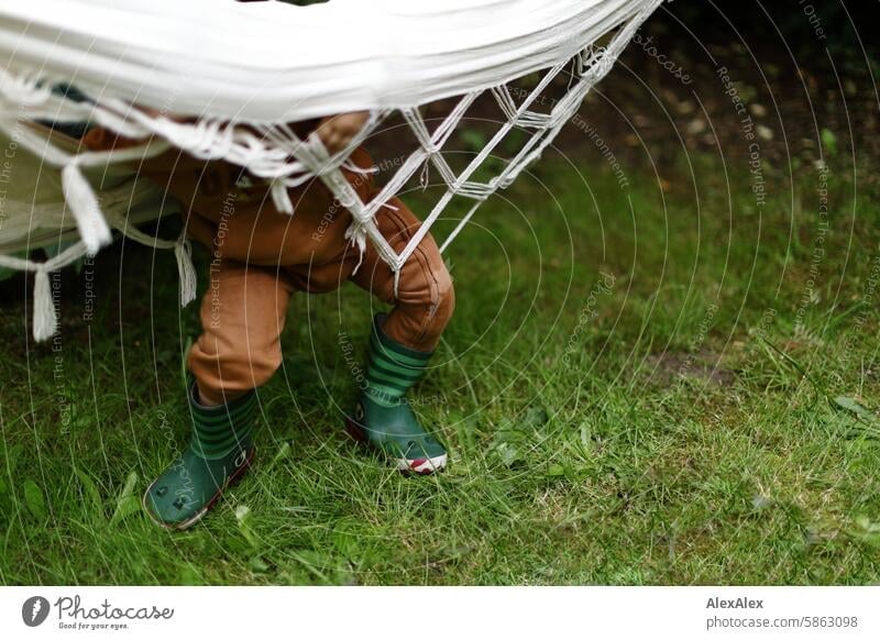 [HH Schregatour24] Ein kleiner Junge in lustig gestalteten Gummistiefeln hat sich in einer Hängematte verheddert und kommt nicht davon los Kind Garten gefangen