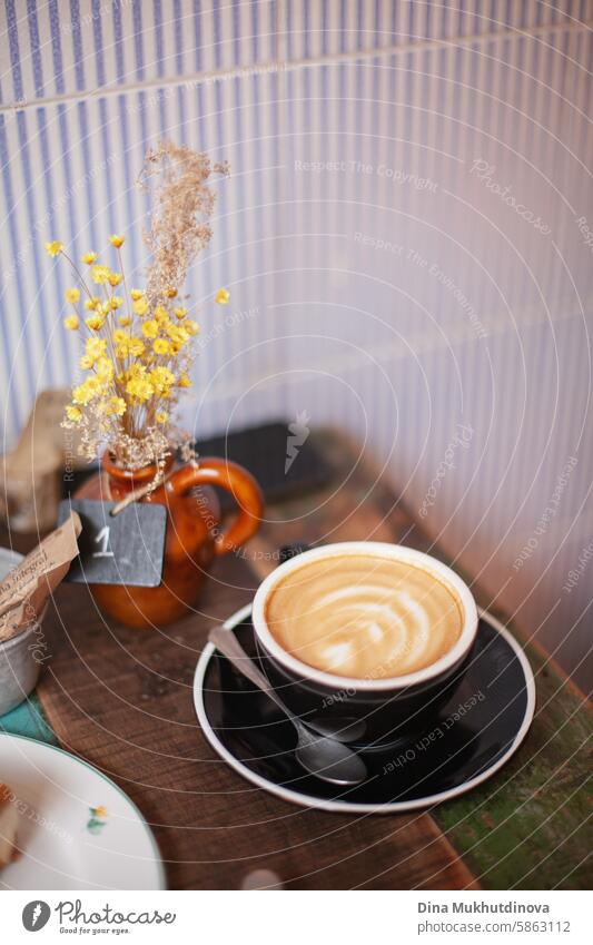 kaffee tasse cappuccino oder flat white mit latte art in einer schwarzen tasse auf einem holztisch im cafe. gemütliches cottage core cafe. Kaffee flach weiß