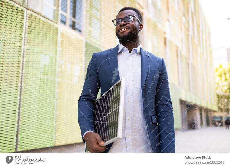 Lächelnder afroamerikanischer Geschäftsmann mit Solarpanel Afroamerikaner Sonnenkollektor Technik & Technologie Innovation nachhaltige Energie urban Straße Mann